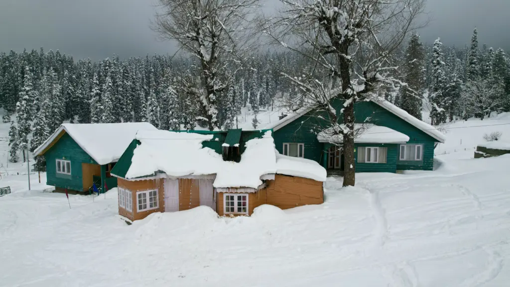 Stunning winter scene in Gulmarg, featuring snow-covered wooden cabins and pine trees.