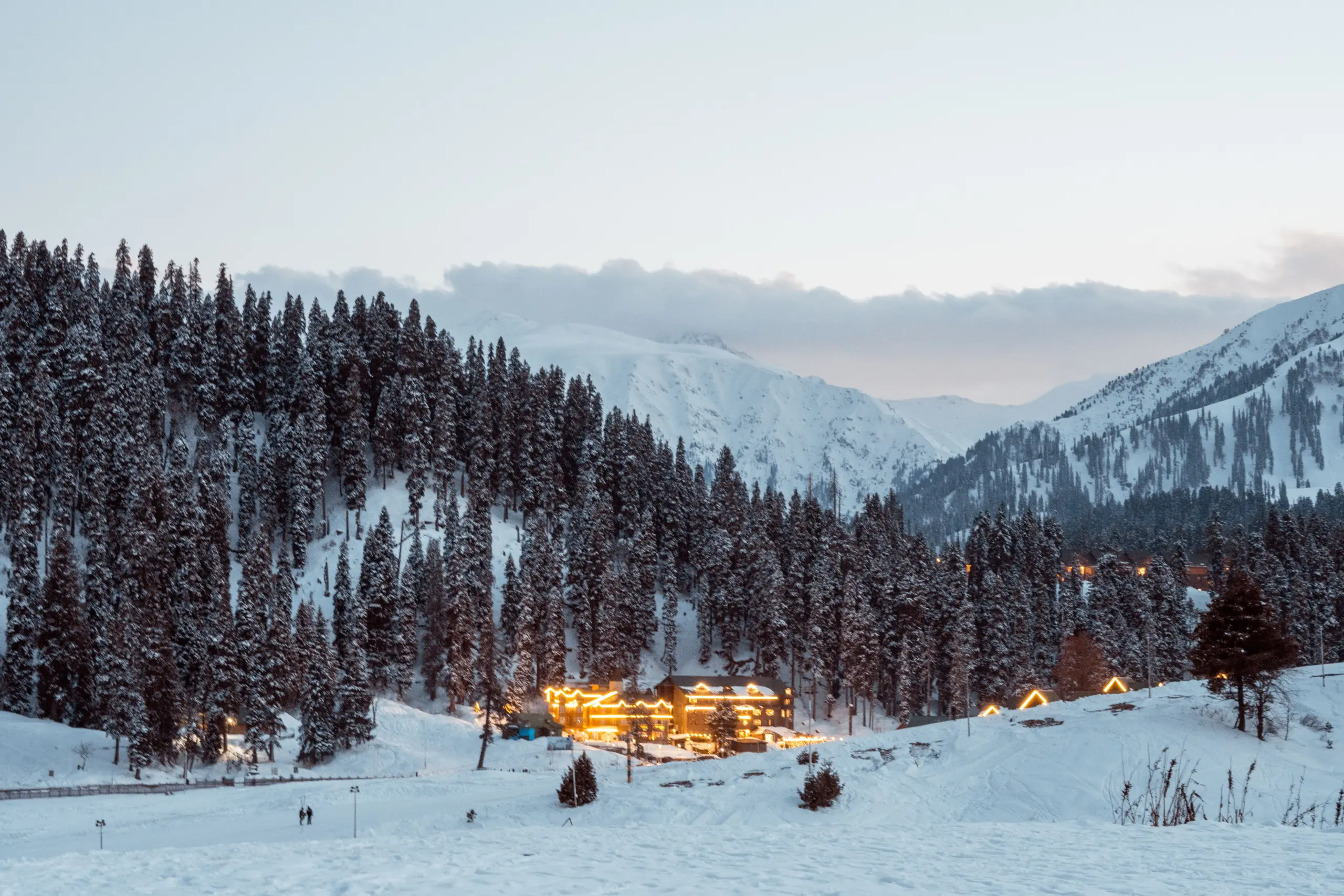 Snow-covered trees and mountains in Gulmarg, Kashmir, create a serene winter landscape.
