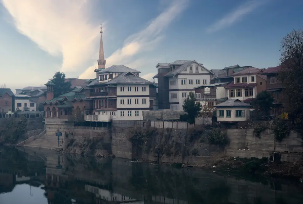 Scenic view of Srinagar's traditional architecture reflected in a calm river during daylight.