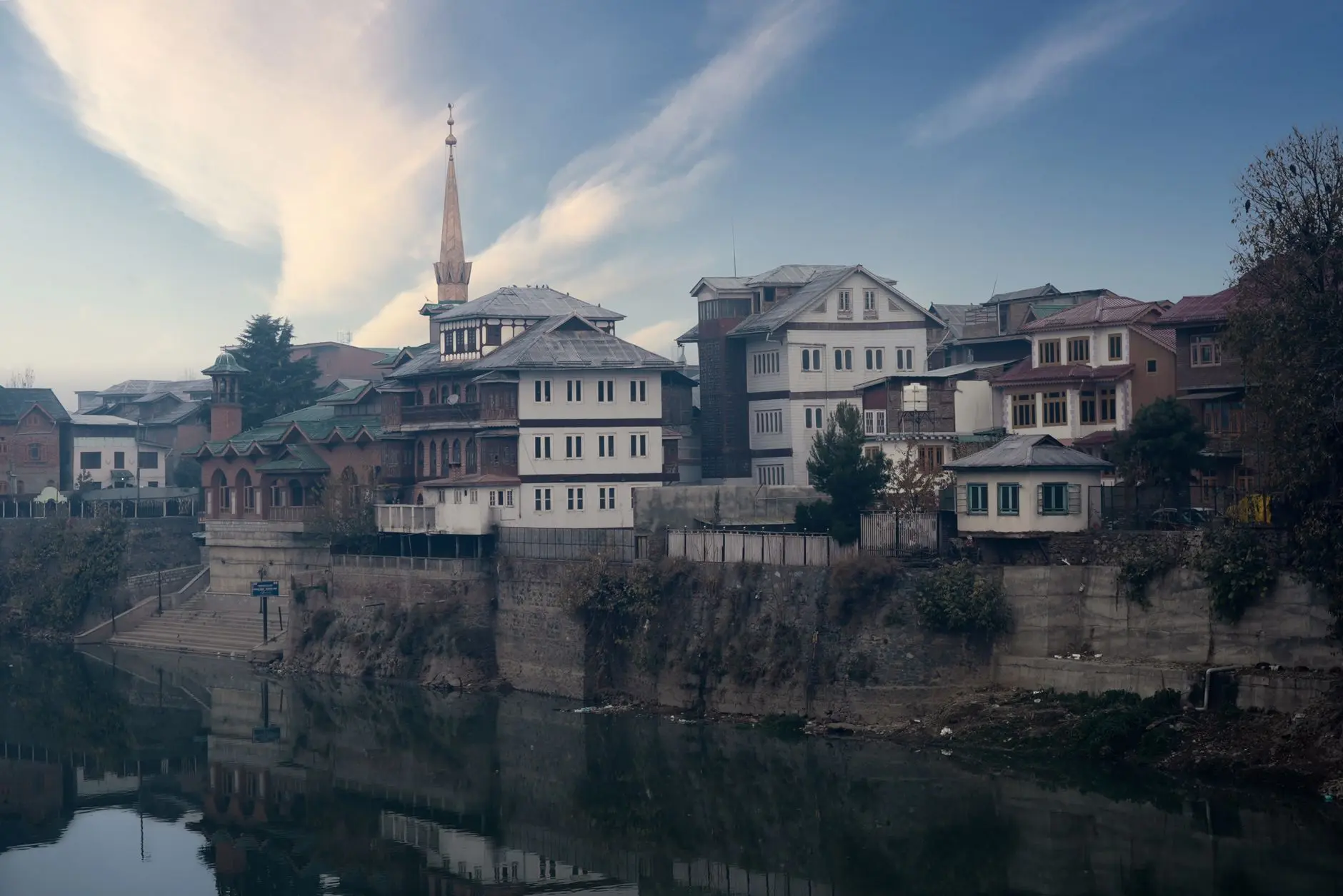 Scenic view of Srinagar's traditional architecture reflected in a calm river during daylight.